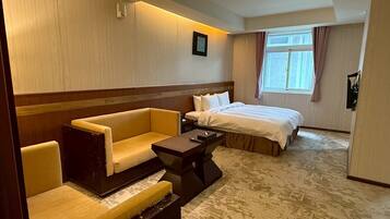 A hotel room with a bed, two sofas, a small table, and a window with curtains.