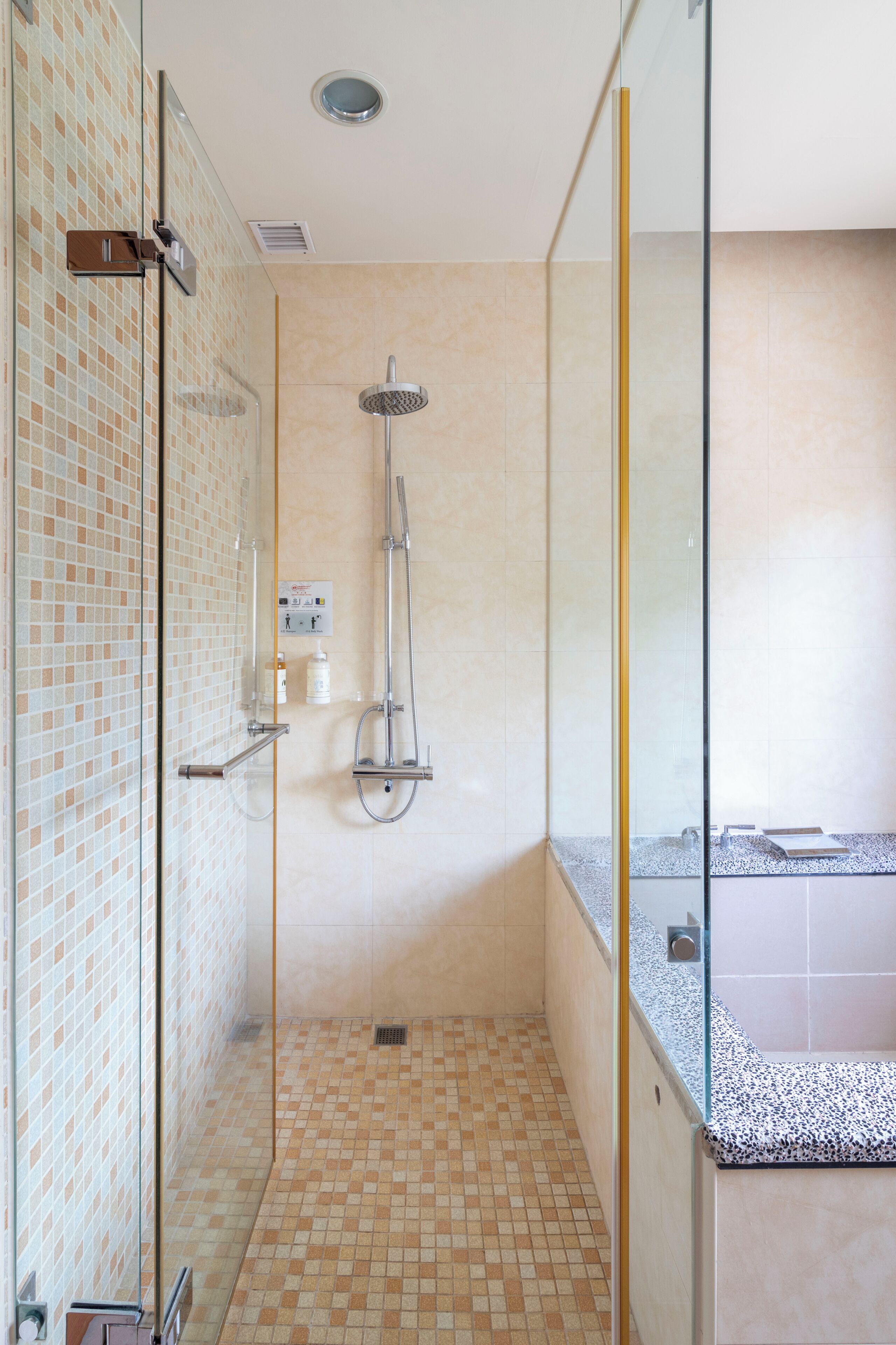 A modern bathroom with a glass shower enclosure, tiled floor, and a visible control panel.
