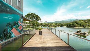 A wooden pier extending over a body of water with a scenic mural on the wall, a railing, and a view of the surrounding landscape.