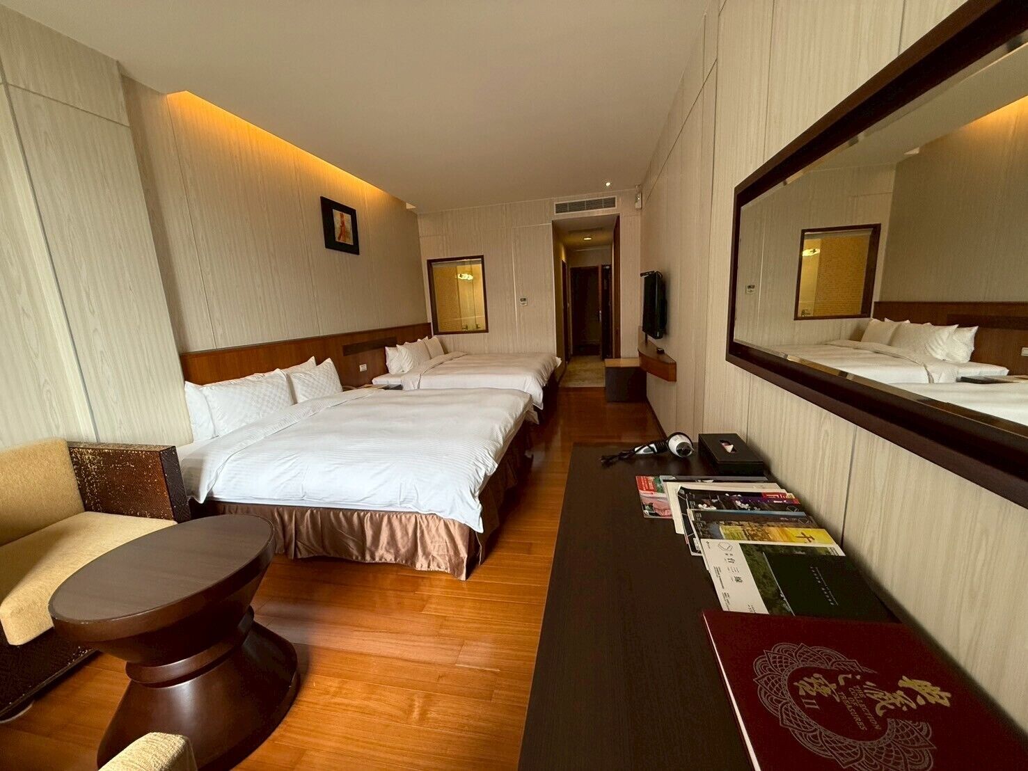 Habitación de hotel con dos camas, un sofá, un escritorio y un espejo grande.