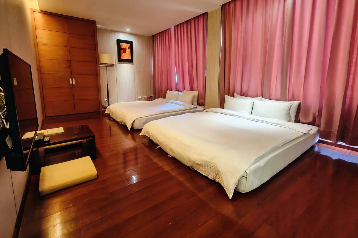 Habitación de hotel con dos camas, suelo de madera, escritorio con silla, armario y un cuadro en la pared.