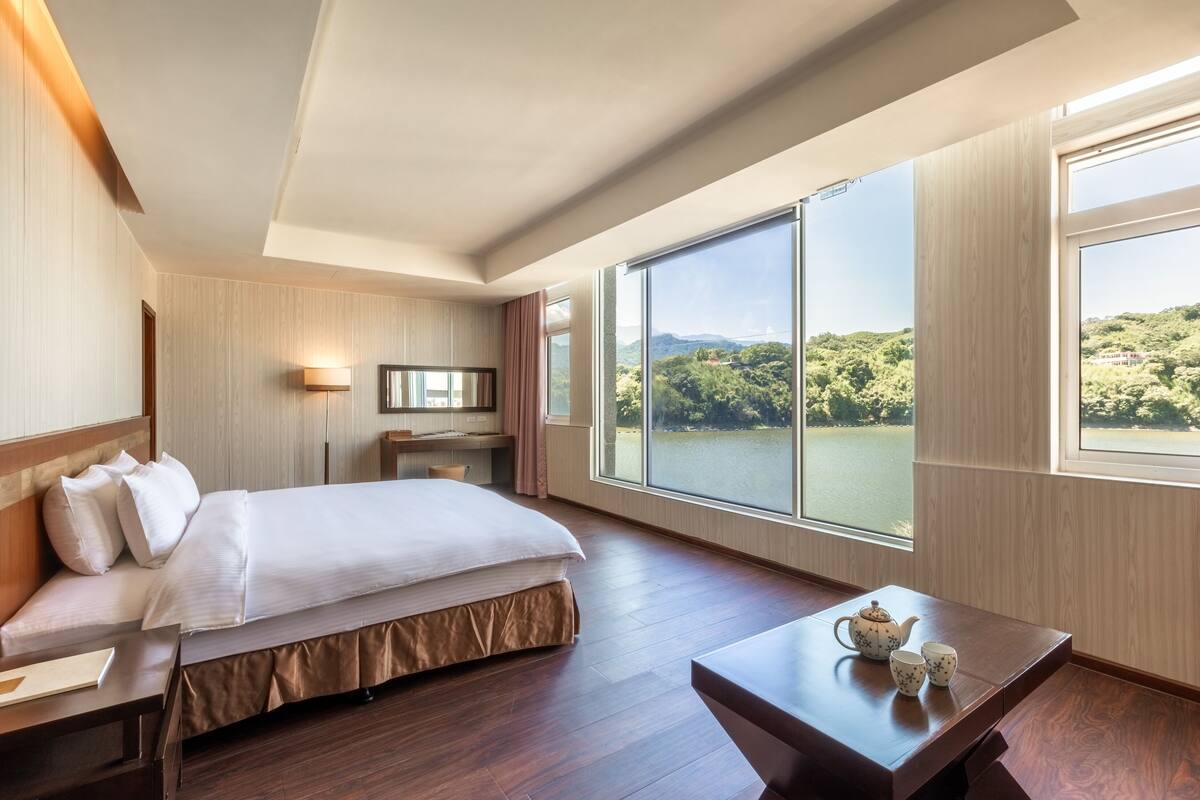 Habitación de hotel con una cama grande, un escritorio y vistas a un lago y montañas.