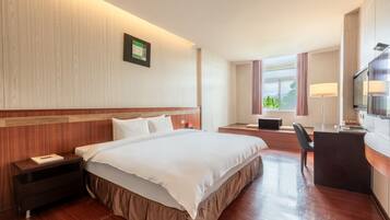 Quarto de hotel com uma cama grande, uma escrivaninha, uma cadeira, uma televisão e uma janela com cortinas.