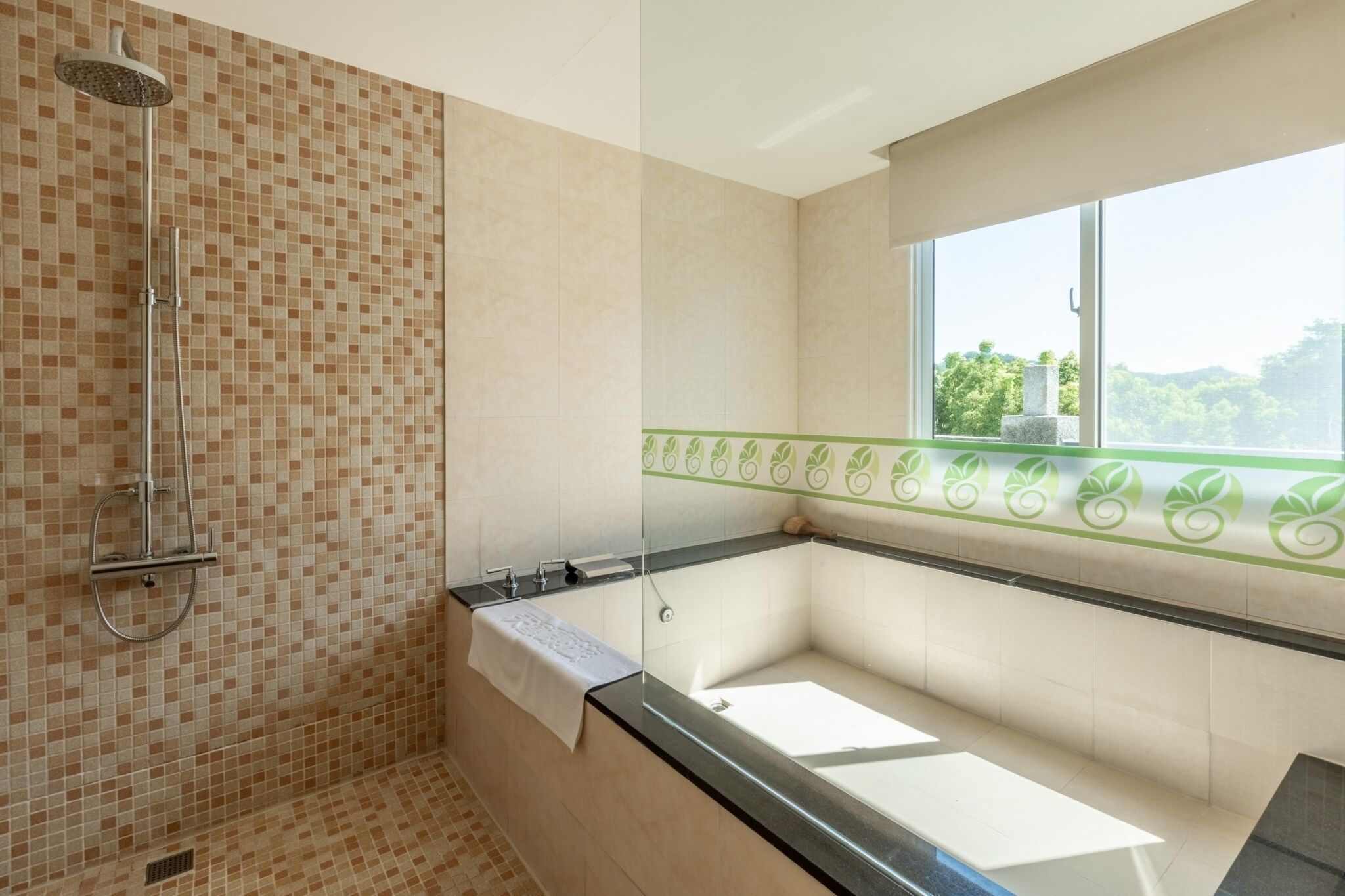 A bathroom with a shower, a bathtub, and a window with a view of greenery.