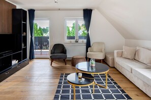 A modern living room with a television, two armchairs, a sofa, a coffee table, and a view of greenery outside.