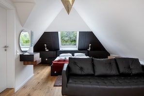 A modern loft bedroom with a large window, a built-in bed, a black sofa, and a wooden floor.