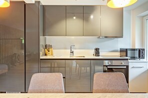 A modern kitchen with a built-in oven, a microwave, and a sink. There are two chairs at the dining table. - Apartment 'Elgit's Bergblick' with Mountain View, Shared Garden and Wi-Fi (Oberried)