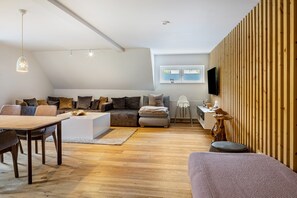 A modern living room with a dining area, a sofa set, a TV mounted on a wooden wall, and a large window. - Apartment 'Elgit's Bergblick' with Mountain View, Shared Garden and Wi-Fi (Oberried)