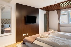 Une chambre à coucher avec un grand lit, un téléviseur fixé au mur, un miroir et une fenêtre avec des rideaux.