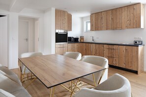 Une cuisine moderne avec des meubles en bois, un four encastré et un coin repas comprenant une table en bois et des chaises blanches.