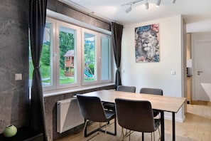 Un comedor con una mesa y sillas, un radiador, una ventana con cortinas y un cuadro en la pared.