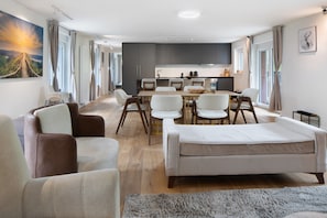 A modern living room with a sofa, chairs, a dining table, and a kitchen area.