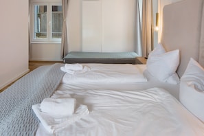 A hotel room with two beds, a window with curtains, a radiator, and a bedside table with a lamp.