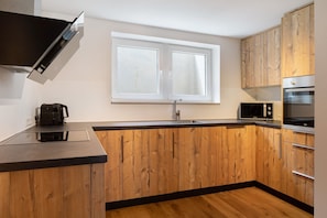 Une cuisine moderne avec des meubles en bois, un plan de travail noir, un four à micro-ondes et un four encastré.