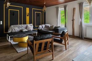 Un salon moderne avec un canapé, des chaises en bois, une table basse et une vue sur l’extérieur.
