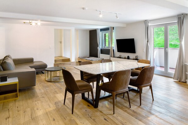 Un salon moderne comprenant un canapé, une table à manger avec des chaises, un téléviseur et une grande fenêtre avec des rideaux.