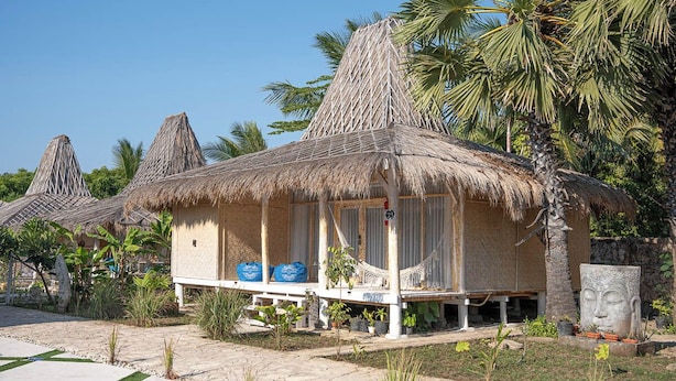 A bungalow-style accommodation with thatched roofs, a porch with seating, and a stone face sculpture. - Sumba Paradise Beach Resort (Palakahembi)