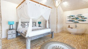 A bedroom with a four-poster bed, a nightstand, a lamp, and a wall-mounted fish painting. - Sumba Paradise Beach Resort (Palakahembi)