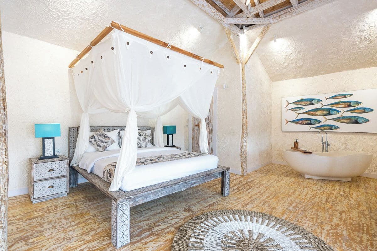 A bedroom with a four-poster bed, a nightstand, a lamp, and a wall-mounted fish painting.