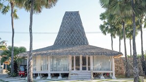 A building with a pyramid-shaped roof, surrounded by palm trees and a patterned lawn. - Sumba Paradise Beach Resort (Palakahembi)