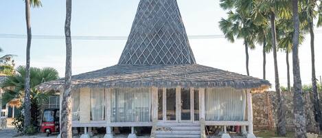 Un edificio con techo en forma de pirámide, rodeado de palmeras y un césped con diseño.