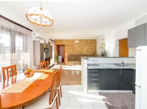 A modern kitchen with a stone backsplash, a dining area with a wooden table and chairs, and a large window with curtains. - Villa Marica (Kastela)