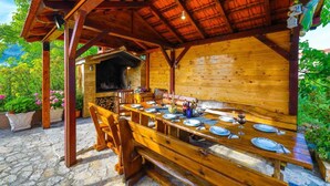 An outdoor wooden dining area with a brick wall, a grill, and potted plants. - Villa Marica (Kastela)
