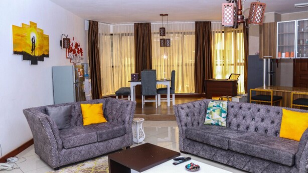 A living room with two grey sofas, a coffee table, and a dining area with a table and chairs. - Myra Residences Kilimani (Nairobi)