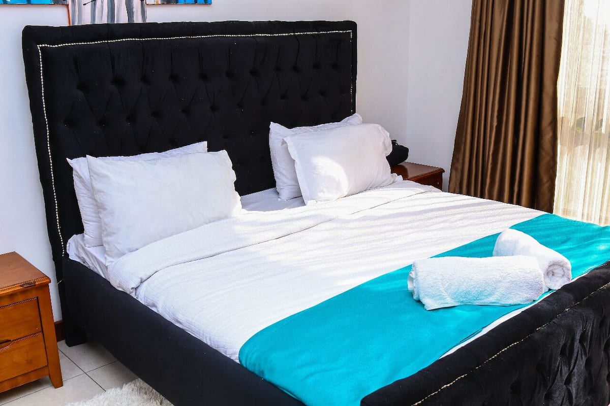 A bed with a black upholstered headboard, white bedding, and a teal accent.