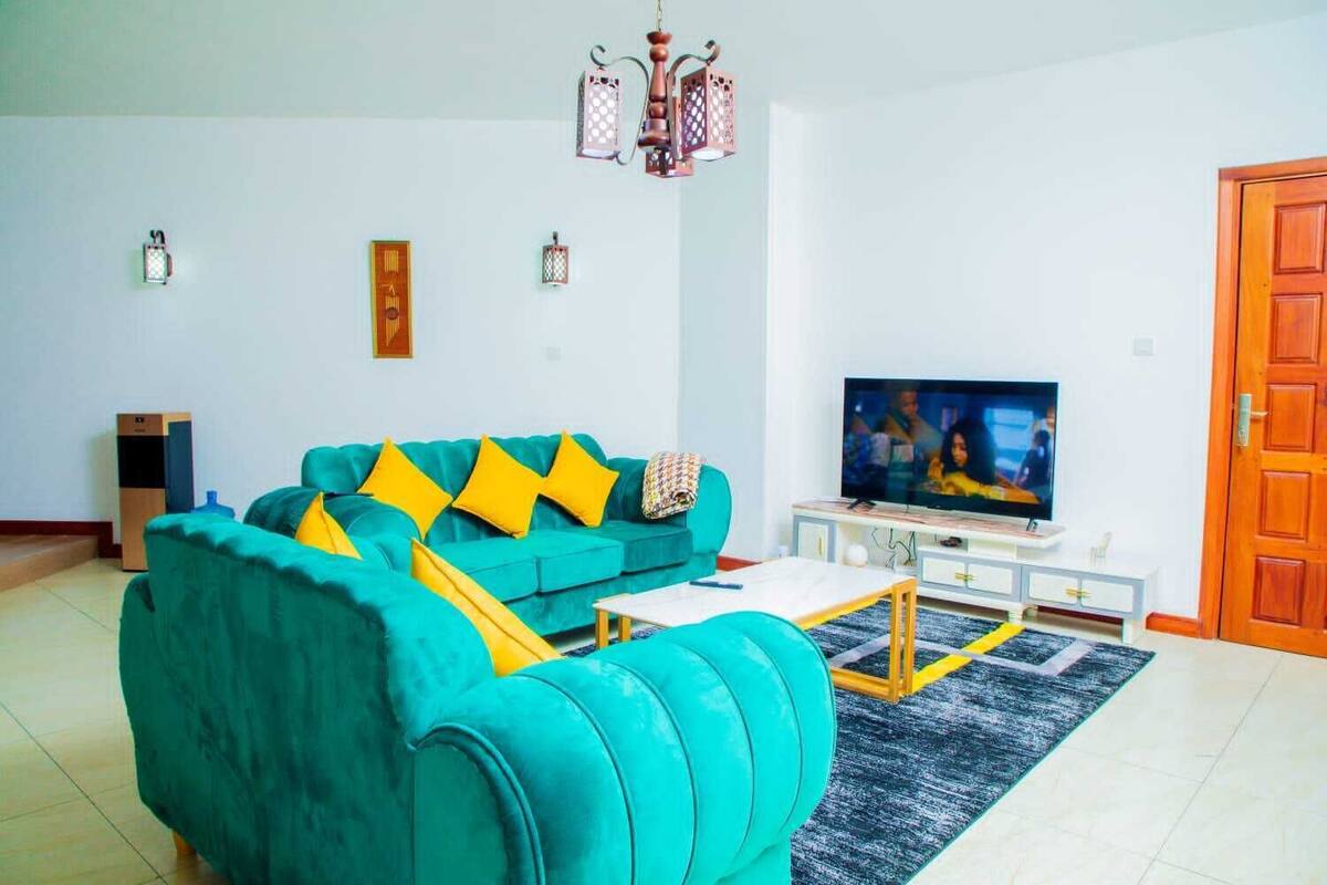 A living room with a teal sofa, yellow cushions, a TV, and a wooden cabinet.