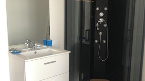 Een moderne badkamer met een glazen douchecabine, een witte wastafel met spiegel en een blauwe prullenbak.
