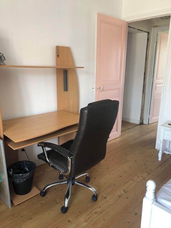 Una habitación con un escritorio de madera, una silla de oficina negra, una mesita de noche blanca y una puerta rosa.