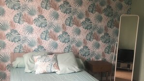 Een slaapkamer met een bed, kussens, een nachtkastje, een spiegel en een houten vloer.