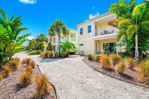 A residential area with a gravel driveway, palm trees, and houses with balconies.