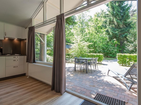 A modern kitchen with a large window, a dining area with outdoor seating, and a view of a garden.