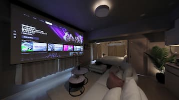 Un salon moderne avec un grand téléviseur à écran plat fixé au mur, un canapé blanc, une petite table basse ronde et une plante en pot.