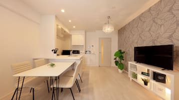 Una cocina moderna con armarios blancos, una mesa de comedor con sillas, una lámpara de araña y un televisor sobre un mueble blanco.