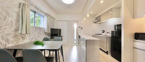 A modern kitchen with a central island, a dining area with chairs, and a TV in the background.