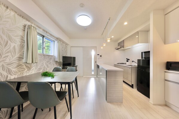 A modern kitchen with a central island, a dining area with chairs, and a TV in the background.