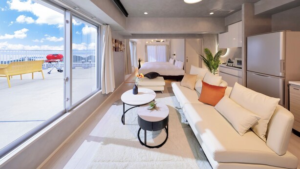 Une chambre d’hôtel moderne avec une grande fenêtre, un canapé, une table basse ronde et un lit.