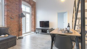 Un salon moderne avec un mur en briques, un téléviseur à écran plat, une table à manger avec des chaises et un canapé sur lequel est posé un livre.