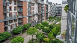 Un immeuble résidentiel à plusieurs étages, doté de balcons, d’une cour intérieure avec des arbres et d’une enseigne indiquant « Now Papier ».