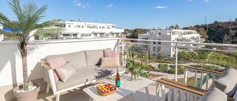 A balcony with a sofa, a table with fruits and a bottle, and a potted plant.