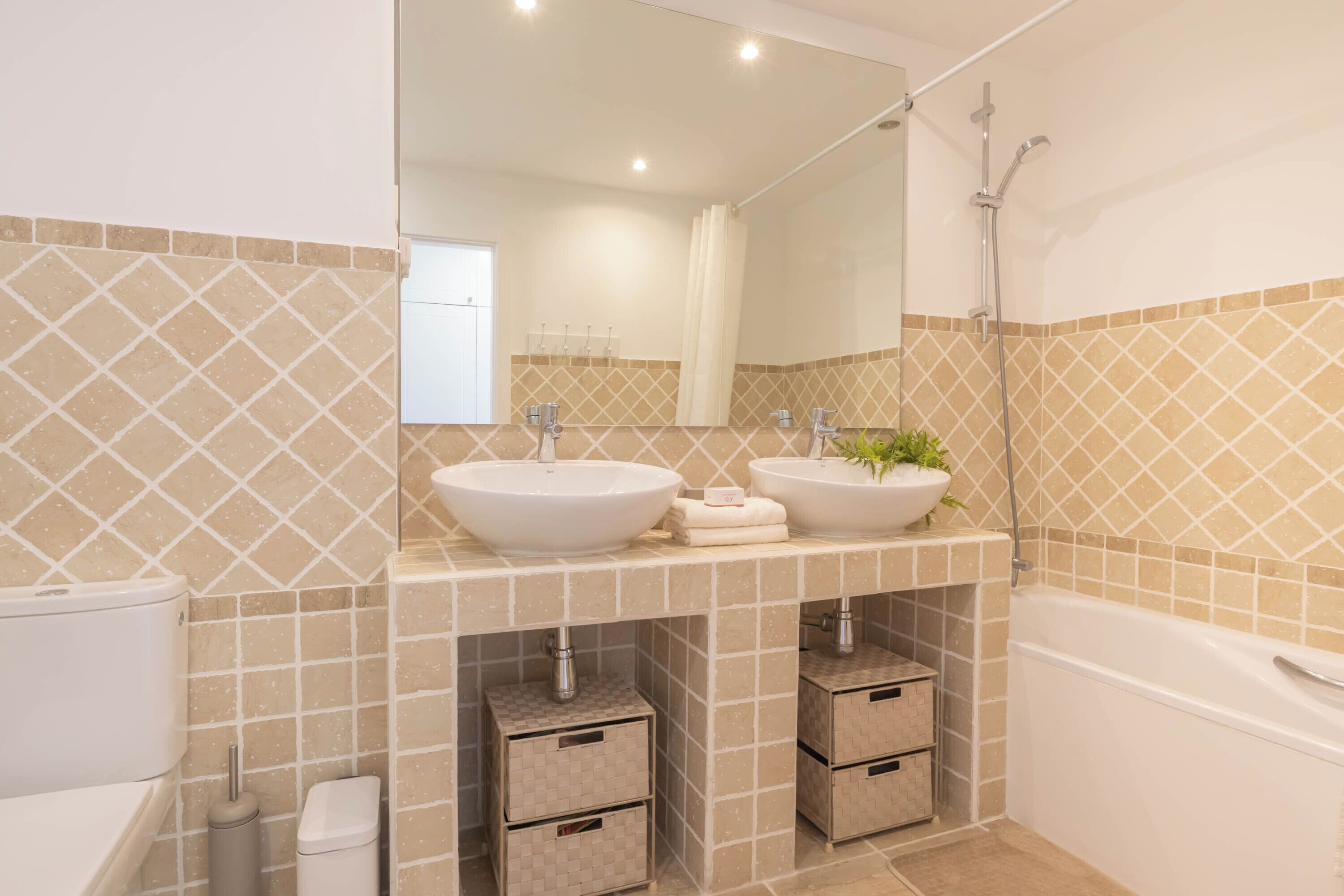 A modern bathroom with two sinks, a shower, and a toilet. There are storage cabinets below the sinks and a mirror above them.