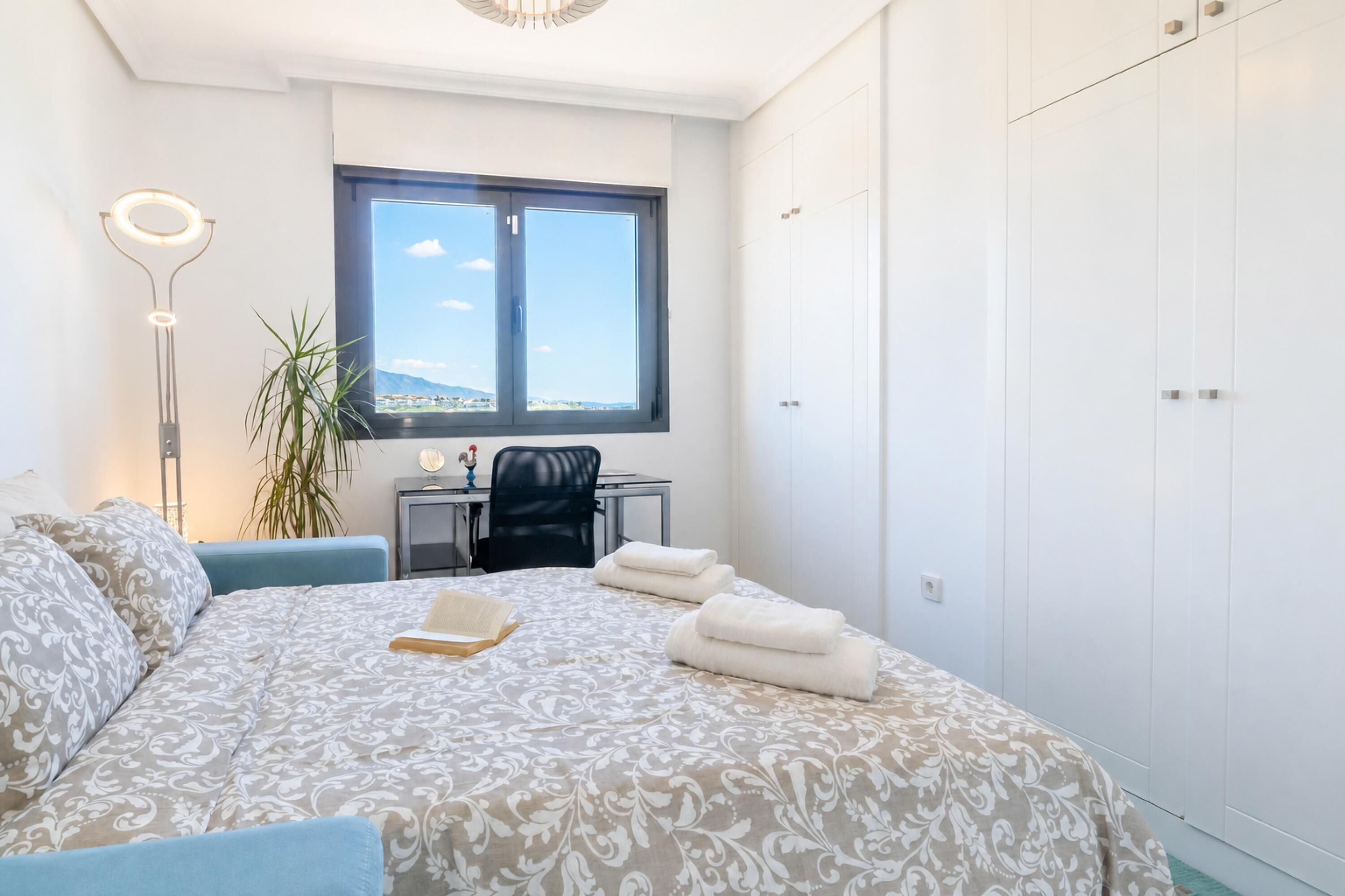A bedroom with a bed, a desk, a chair, a potted plant, and a wardrobe.