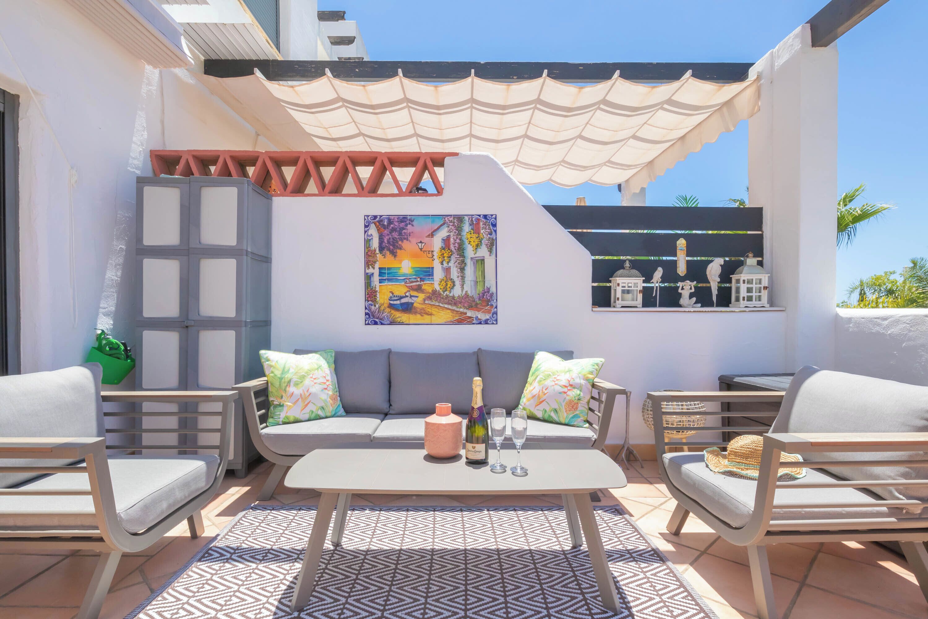 A sunlit patio with a sofa, chairs, a table, and a decorative wall.