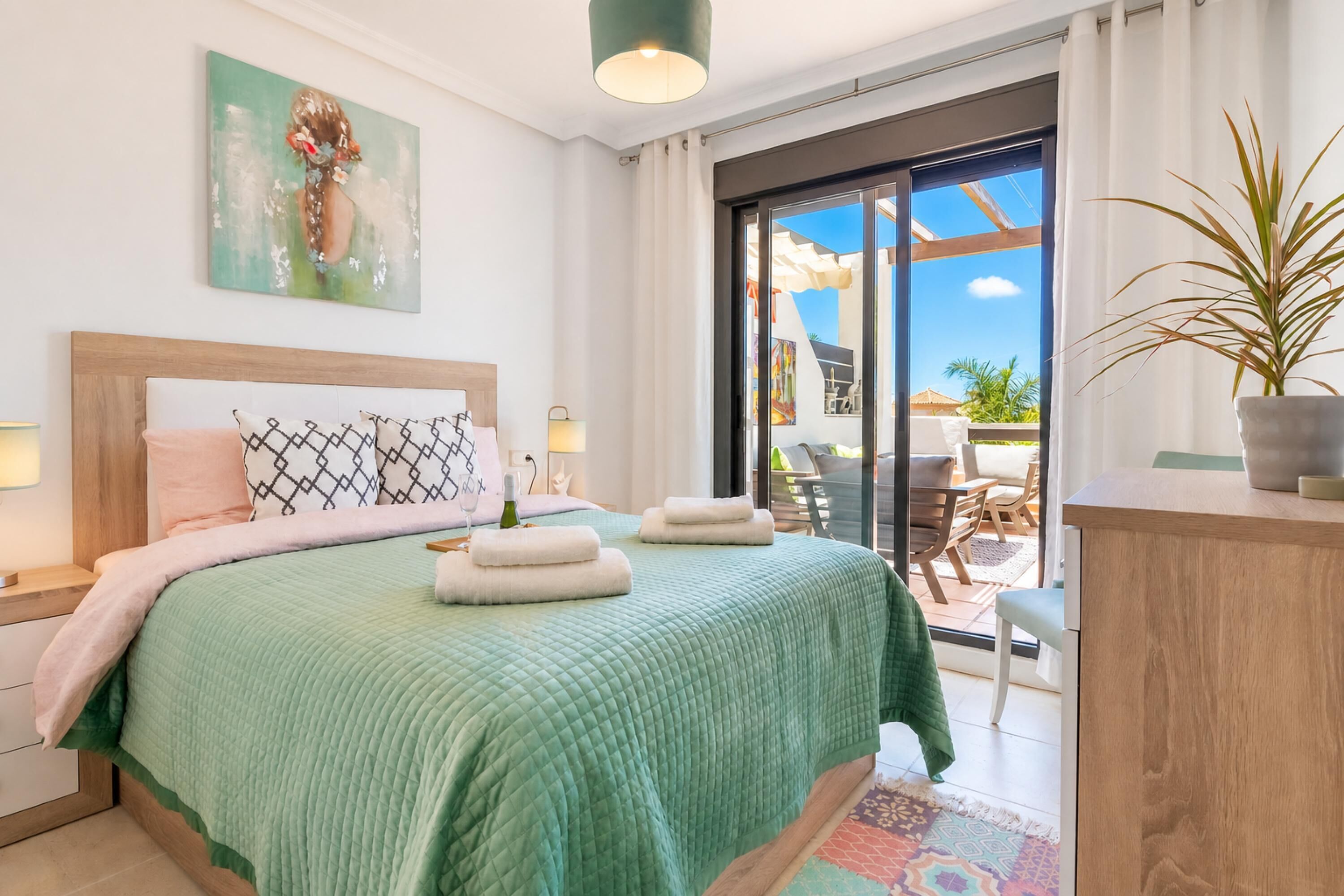 Una camera da letto con un letto, un quadro, una pianta in vaso e vista sull'esterno.