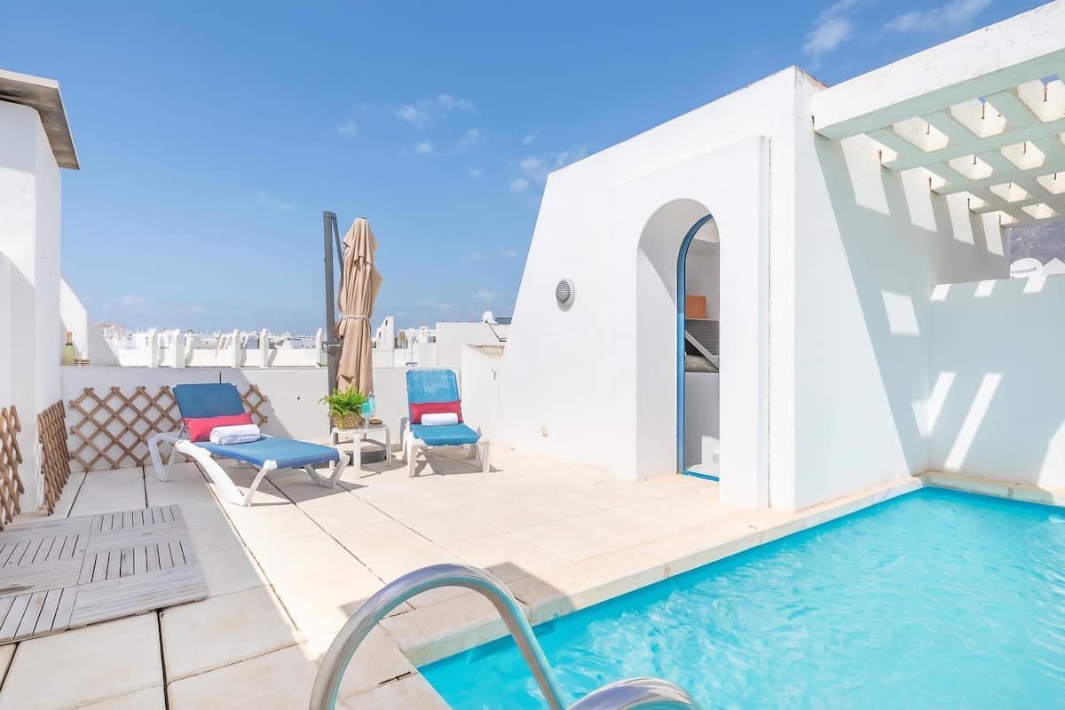 A rooftop pool area with lounge chairs, a pool, and a view of the city.