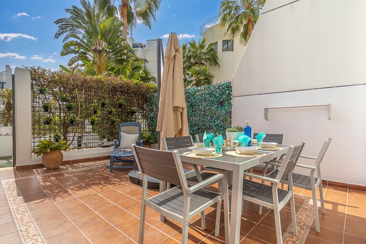 A patio with a table set for dining, surrounded by chairs, a potted plant, and a hanging chair.