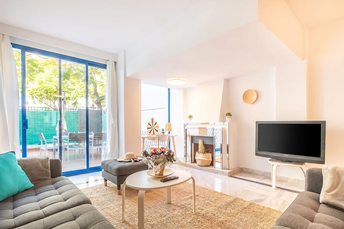 A modern living room with a sofa, a coffee table, a flat-screen TV, and a sliding glass door leading to an outdoor area.